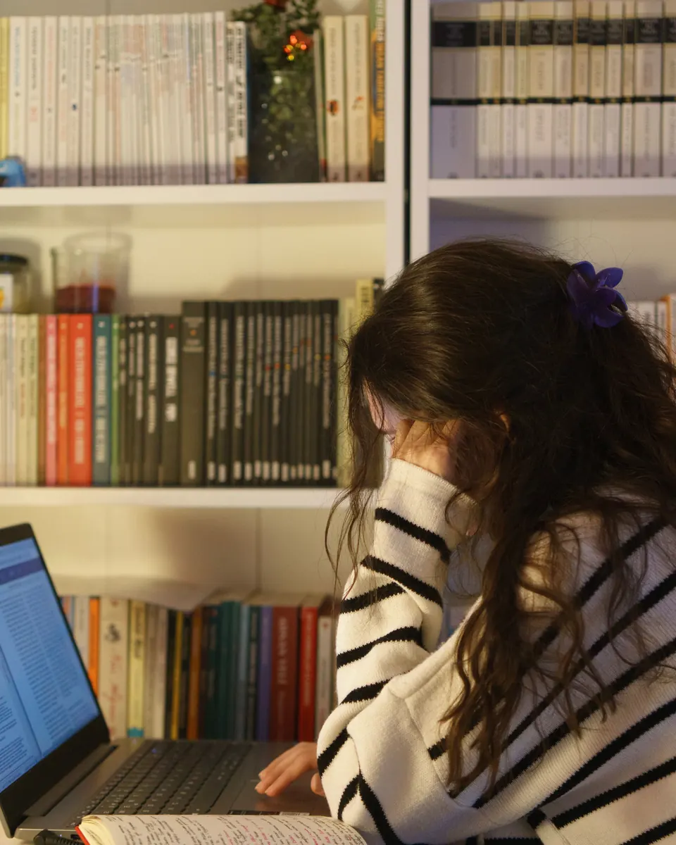 Estudiante consulta una laptop y un cuaderno abierto frente a una biblioteca